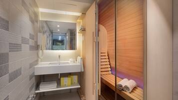 Un baño moderno con un espejo grande, lavamanos blanco y banco de sauna de madera.