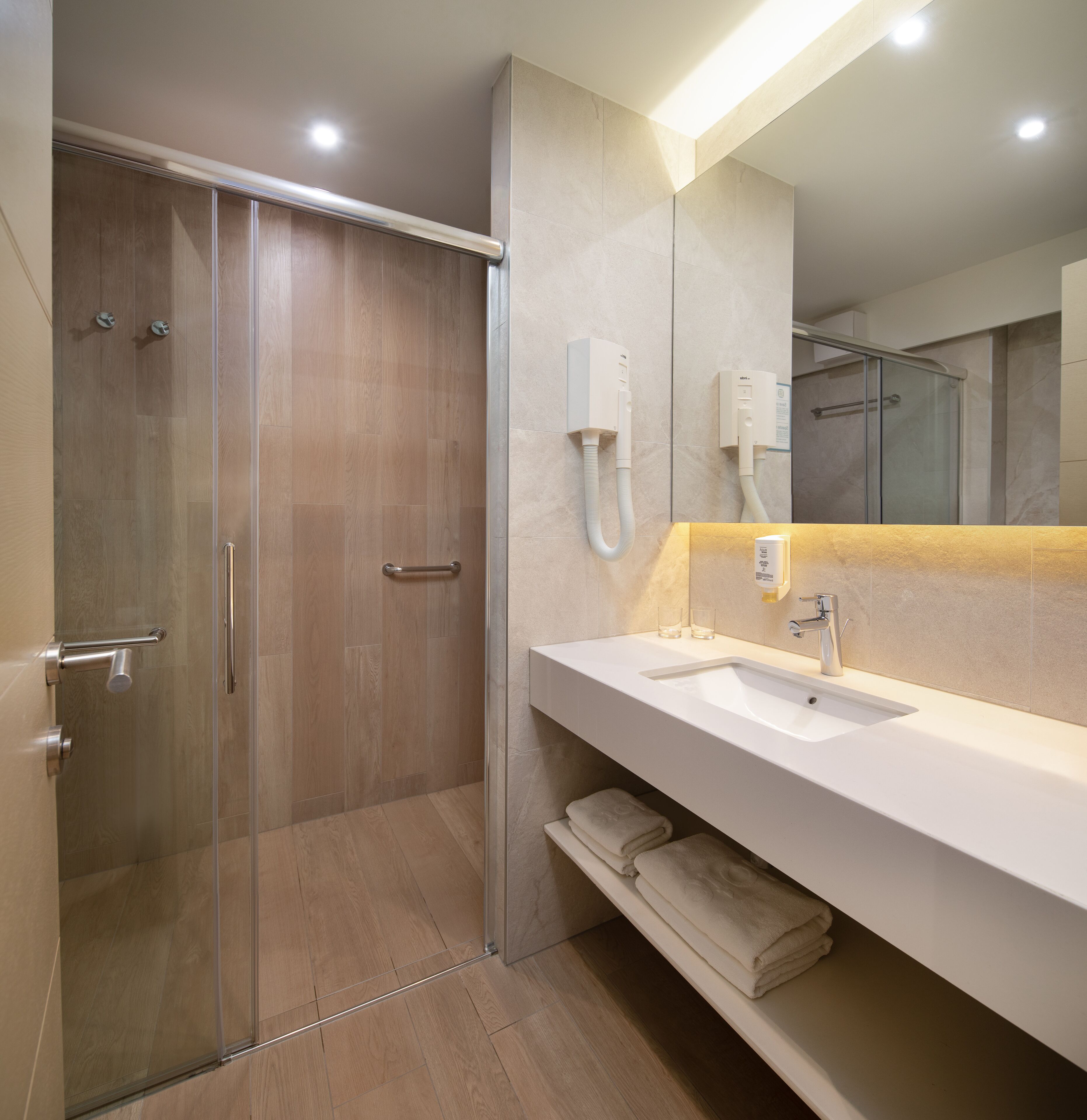 Une salle de bain moderne avec une douche à l’italienne en verre, un lavabo blanc et un grand miroir.