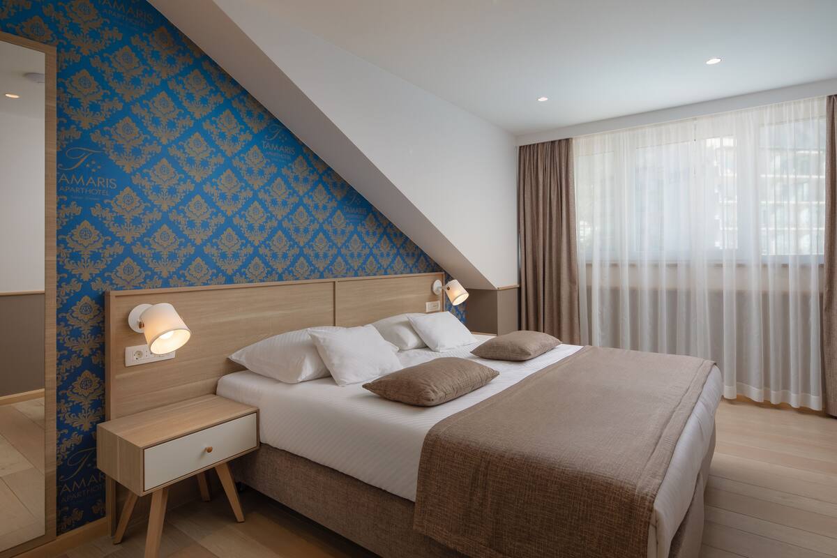 A modern bedroom with a sloped ceiling, a large bed with white bedding, two bedside lamps, and a nightstand.