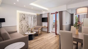 Una moderna camera d'albergo con divano, tavolo da pranzo e sedie, televisione a schermo piatto e vista sull'esterno.