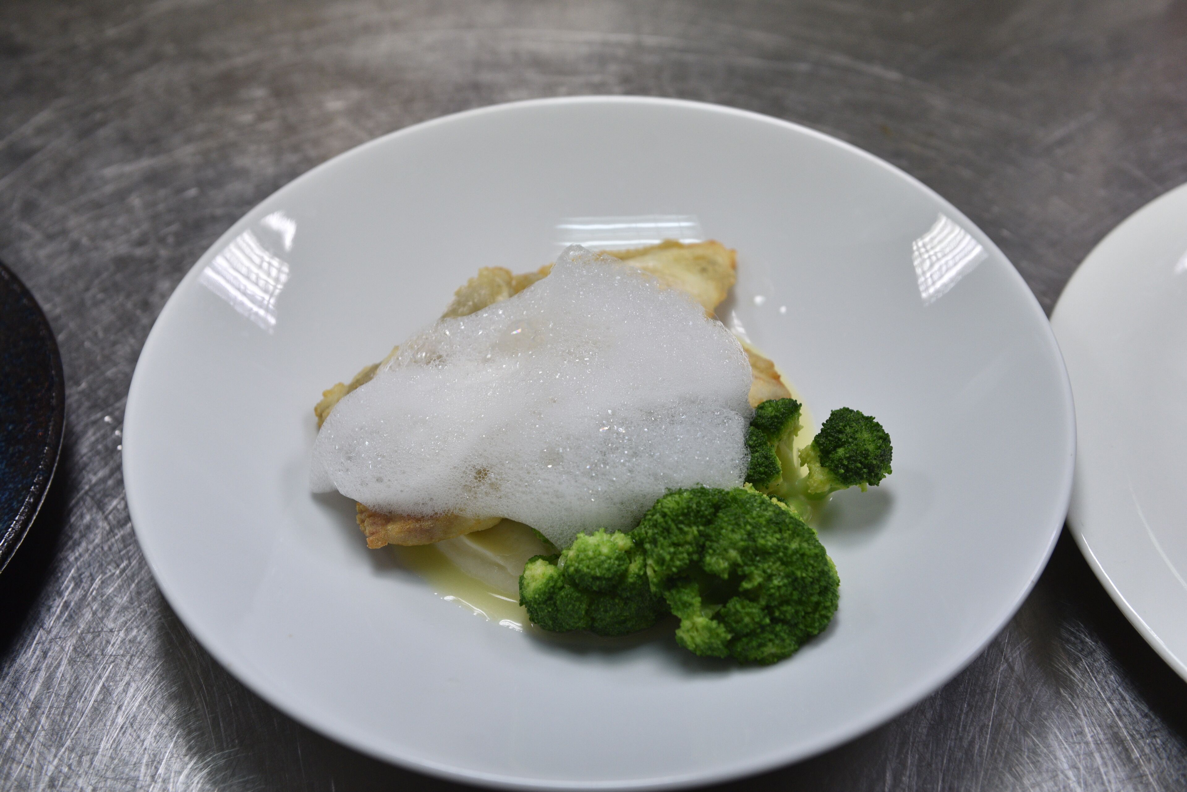 A plate with a piece of fish, a dollop of cream, and broccoli on a white plate.