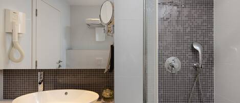 Een moderne badkamer met een groot wit wastafelmeubel, een douche met glazen wand en een betegelde spatwand.
