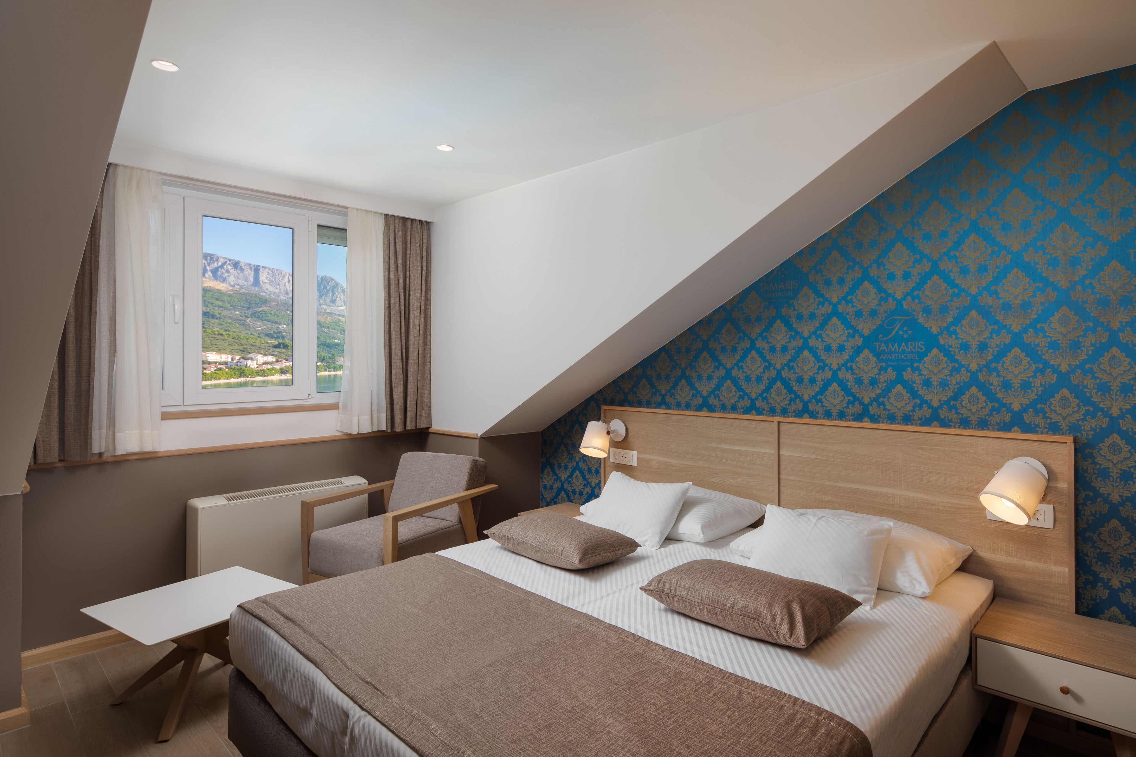 A bedroom with a bed, bedside tables, a desk, a chair, and a window with curtains.