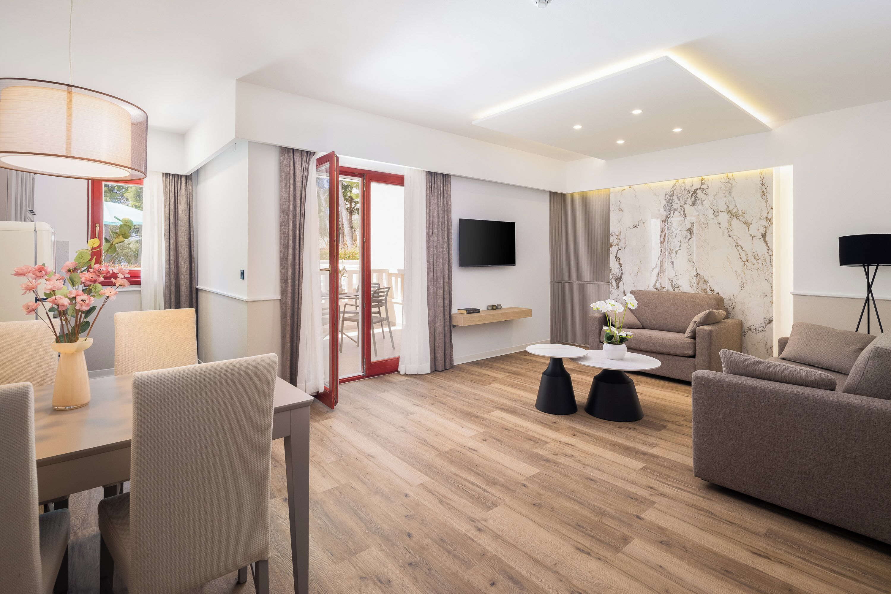 Una sala de estar moderna con un sofá, una mesa de comedor con sillas, un televisor montado en la pared y piso de madera.