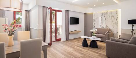 Una sala de estar moderna con un sofá, una mesa de comedor con sillas, un televisor montado en la pared y piso de madera.