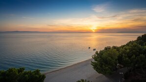 Vista costiera con spiaggia, mare calmo e tramonto.