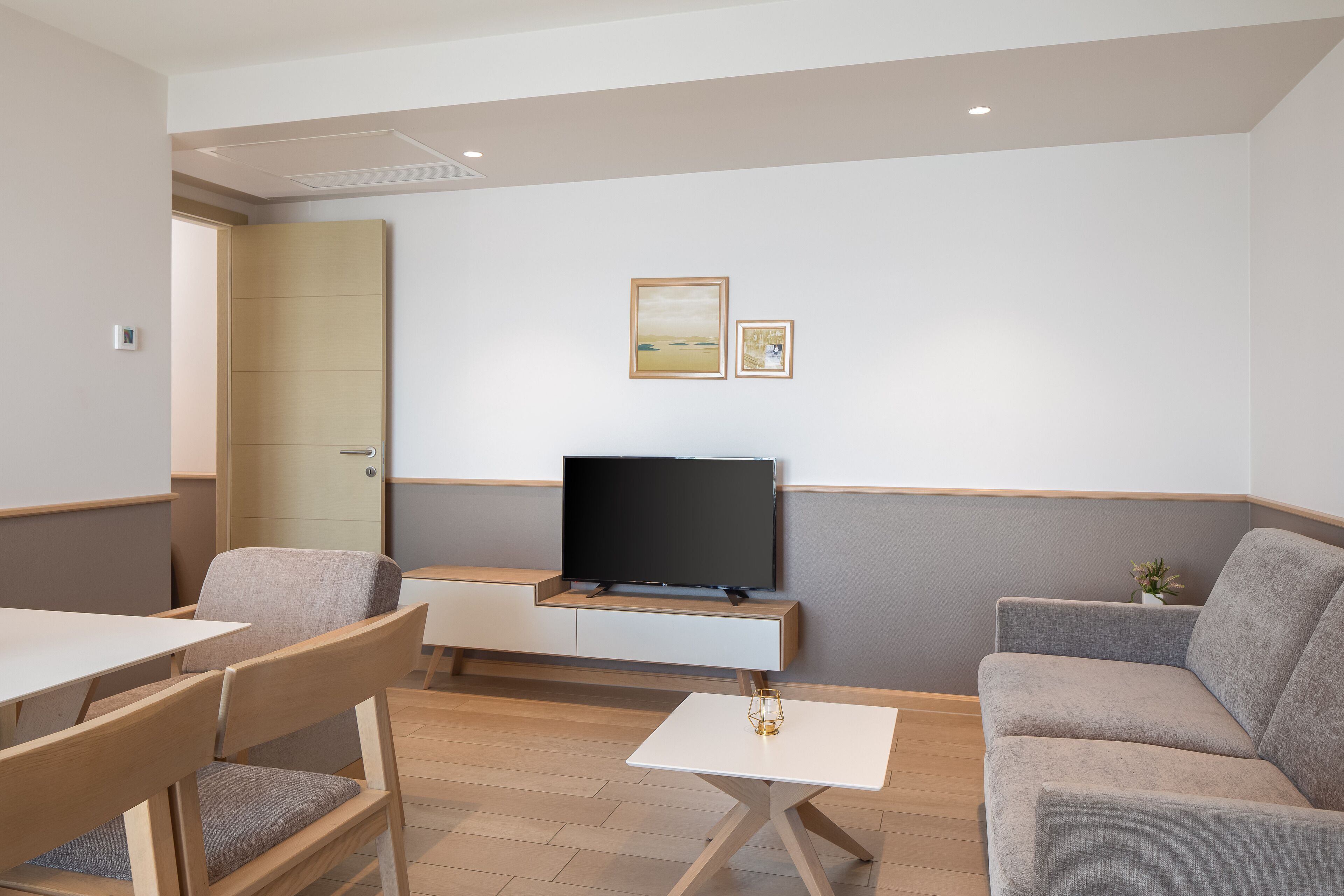 A modern living room with a flat-screen TV, a sofa, a dining table, and chairs.