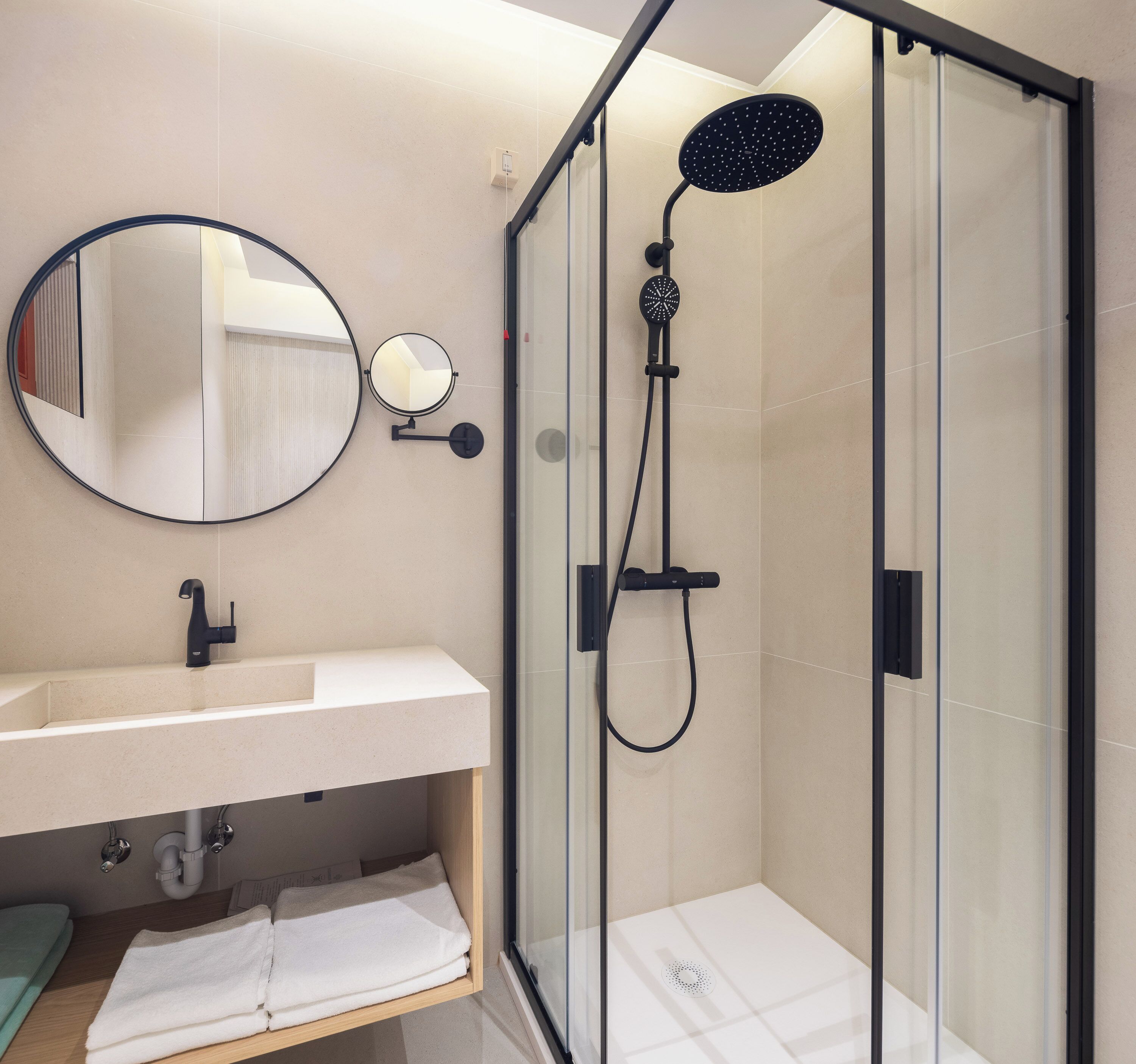 A modern bathroom with a glass-enclosed shower, a round mirror, a white sink, and a towel rack.