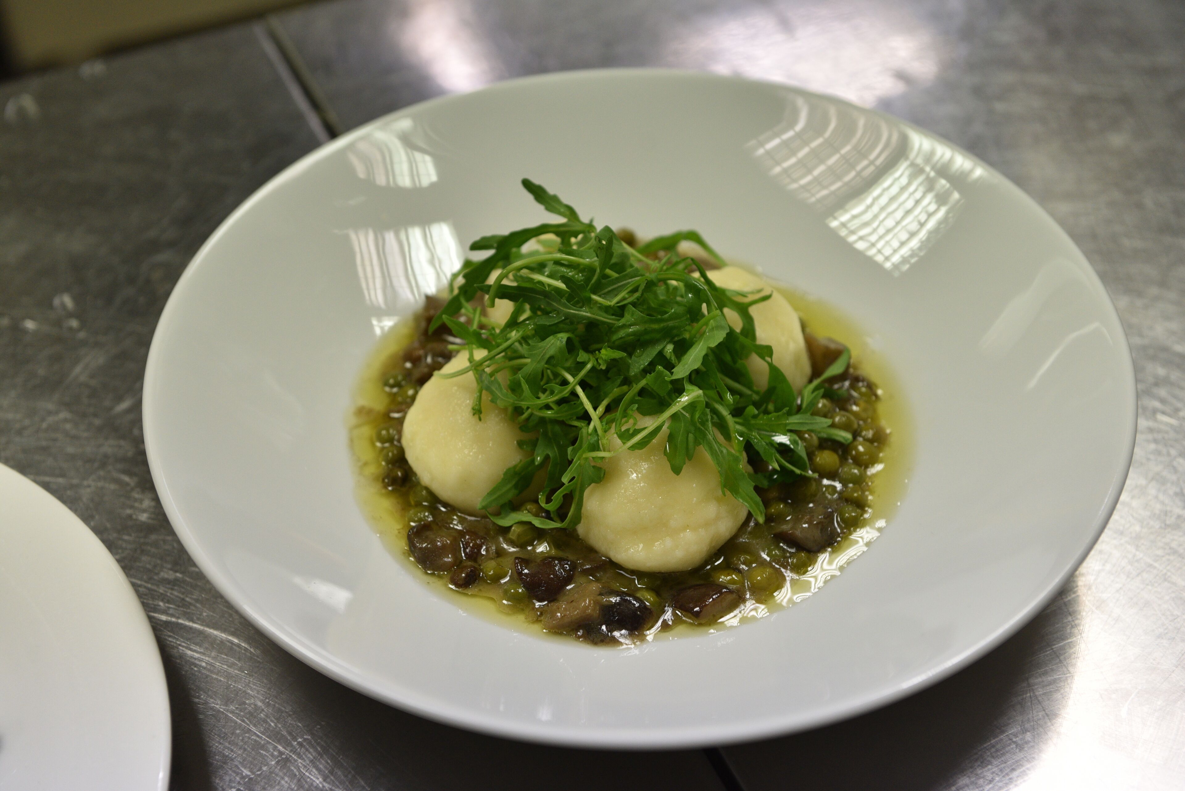 En hvid tallerken med to dumplings, grønt pynt og grøn sauce.