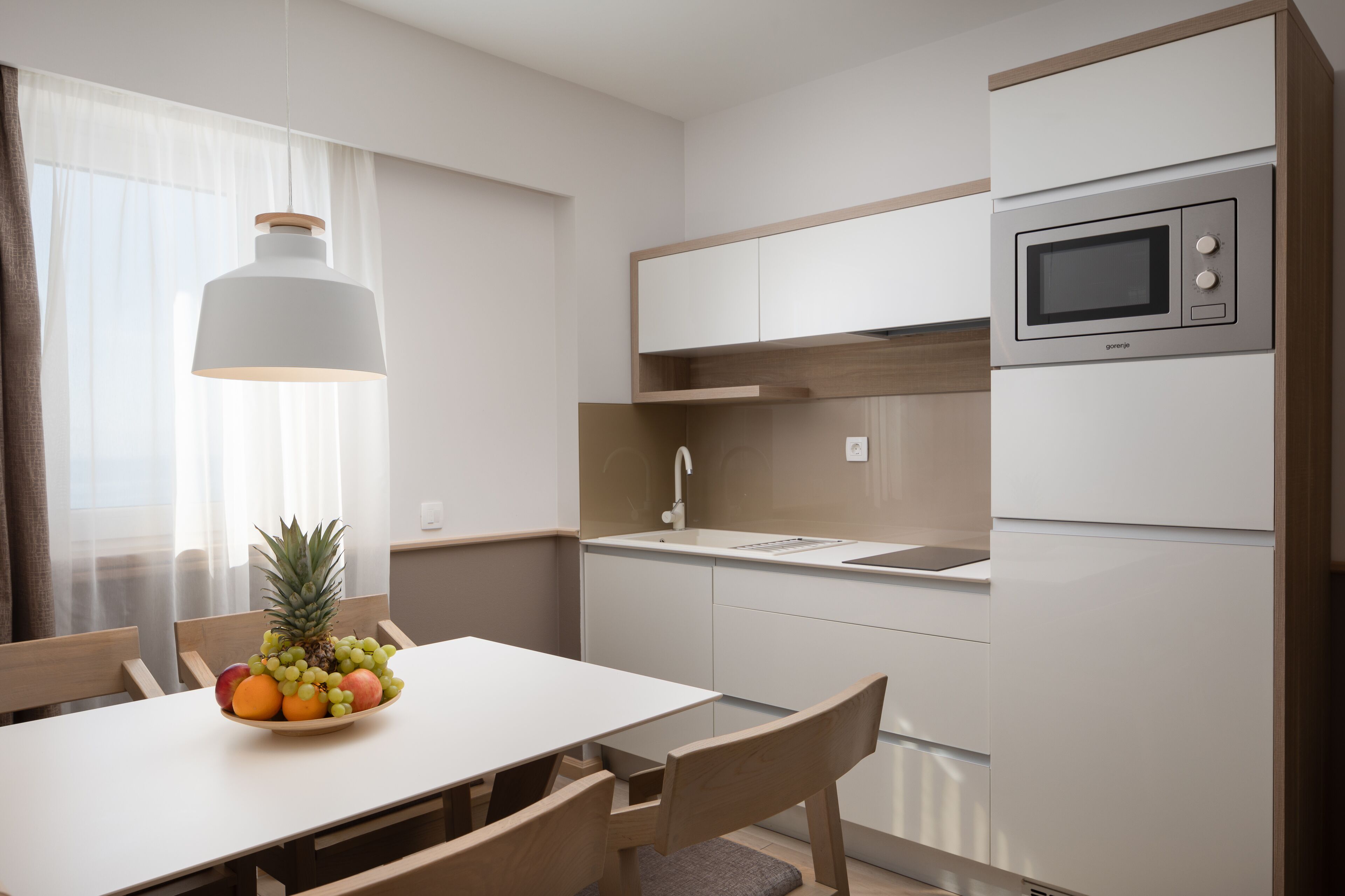 A modern kitchen with a dining area, featuring a microwave, sink, and a bowl of fruit on the table.