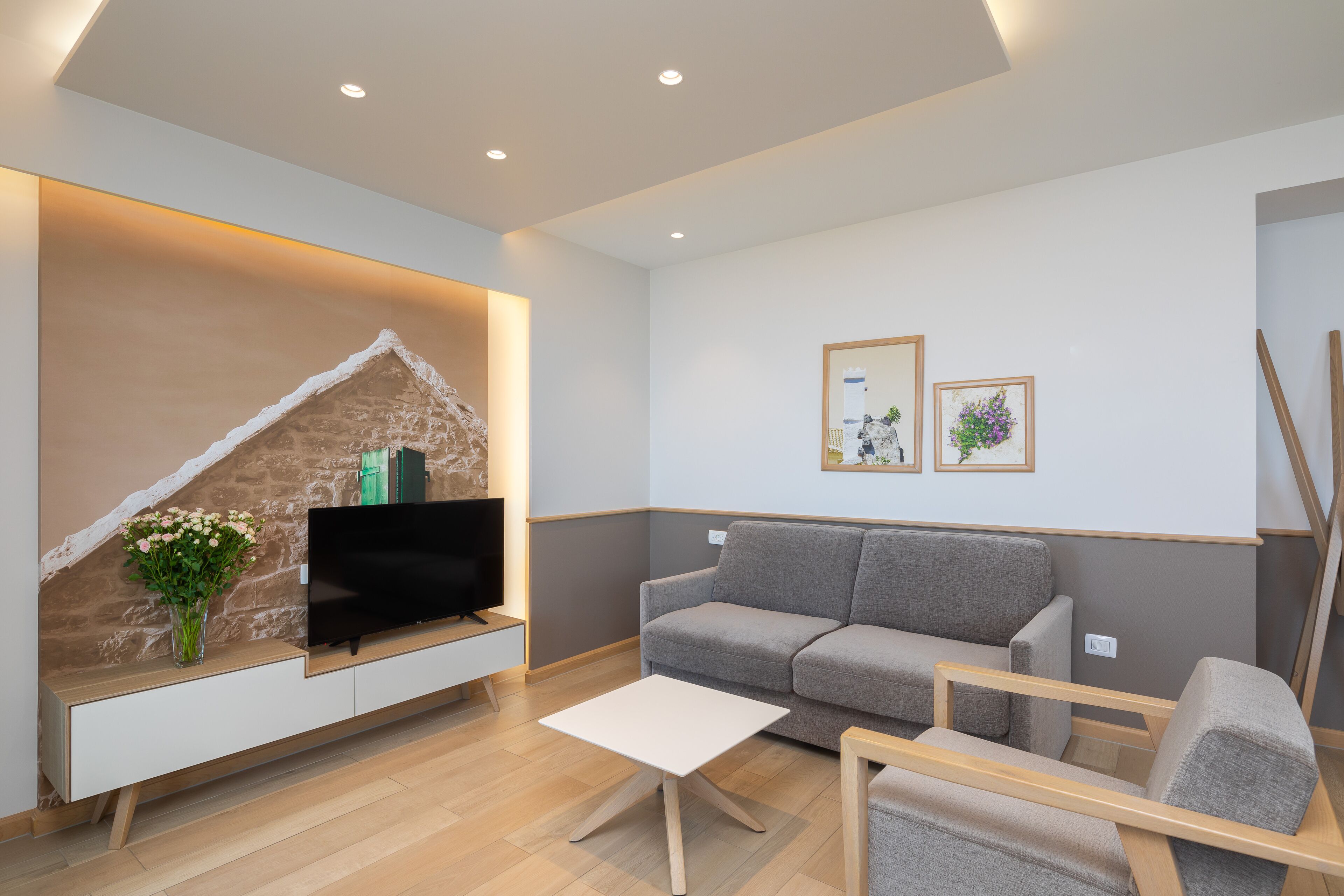 A modern living room with a flat-screen TV, grey sofa, white coffee table, and a stone accent wall.