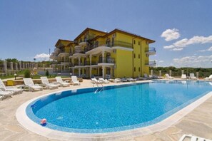 Una piscina grande con sillones de descanso y un edificio amarillo con balcones al fondo.
