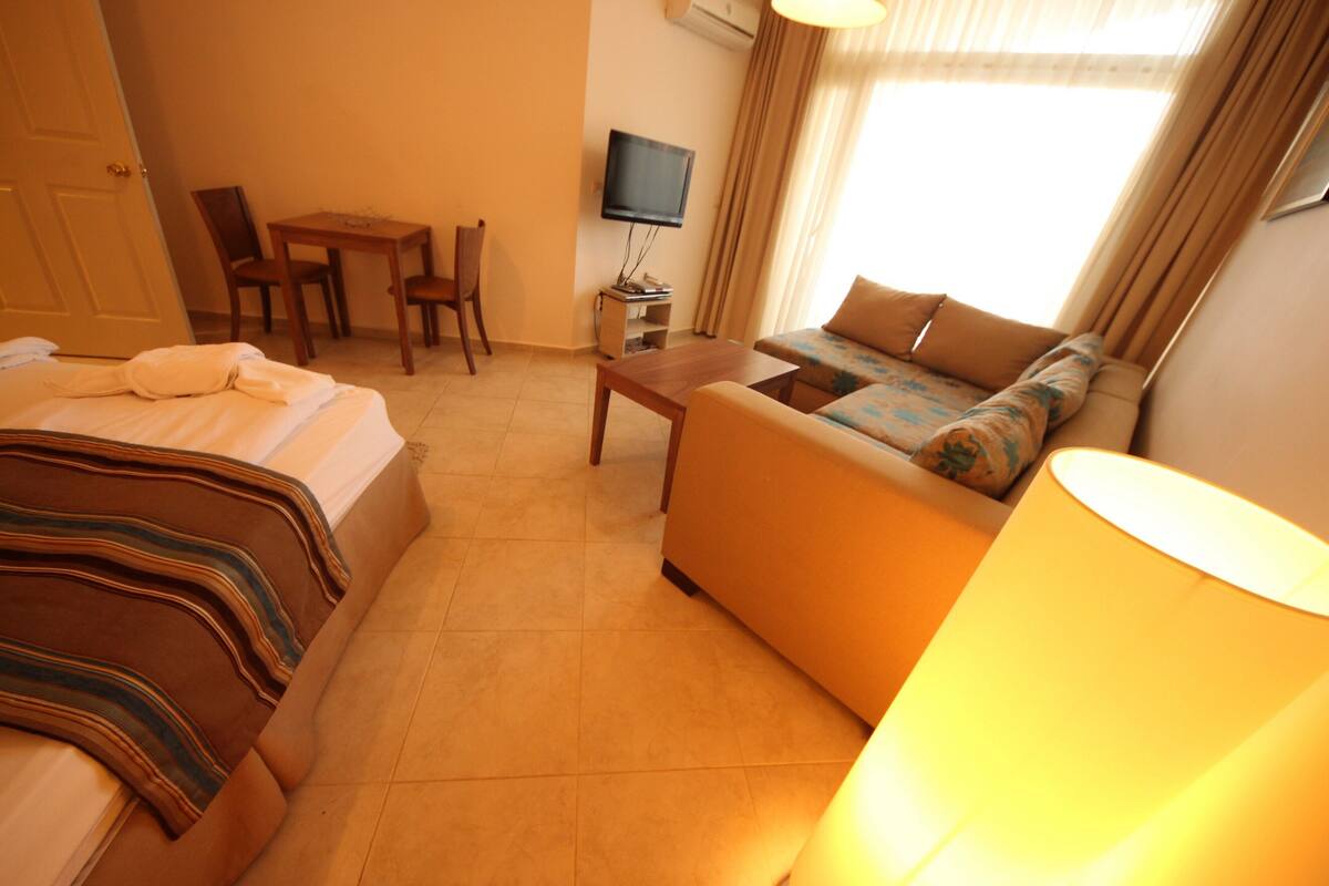A hotel room with a bed, a sofa, a table, a TV, and a lamp.
