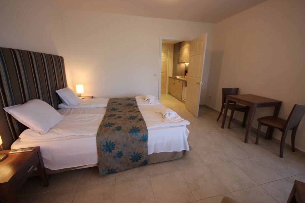 A hotel room with a bed, bedside table, lamp, and a small desk with a chair.