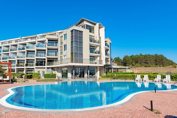 A modern hotel with a swimming pool, multiple balconies, and a landscaped garden.