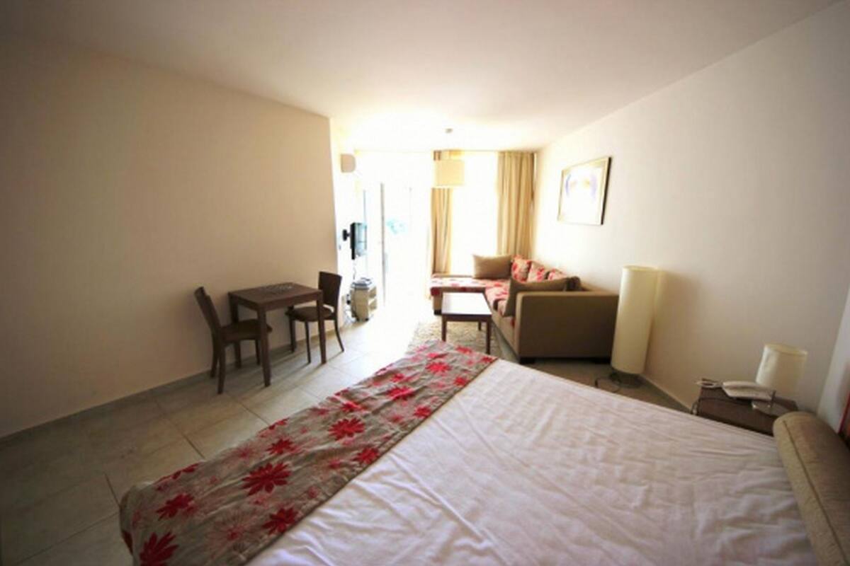 A hotel room with a bed, a desk, a chair, a sofa, and a lamp.