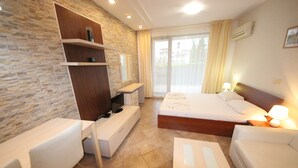 A modern hotel room with a stone accent wall, a large bed, a desk, and a sofa.