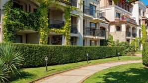 A multi-story residential building with balconies, a paved pathway, and well-maintained greenery.