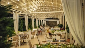 An outdoor dining area with tables and chairs, a covered walkway, and potted plants.