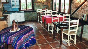 A rustic dining area with wooden tables and chairs, a patterned tablecloth, and a copper pitcher on the table. - Aristieta (Ajangiz)
