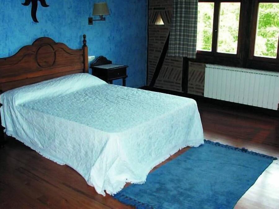 Quarto com cama de madeira, tapete azul e janela com cortinas.