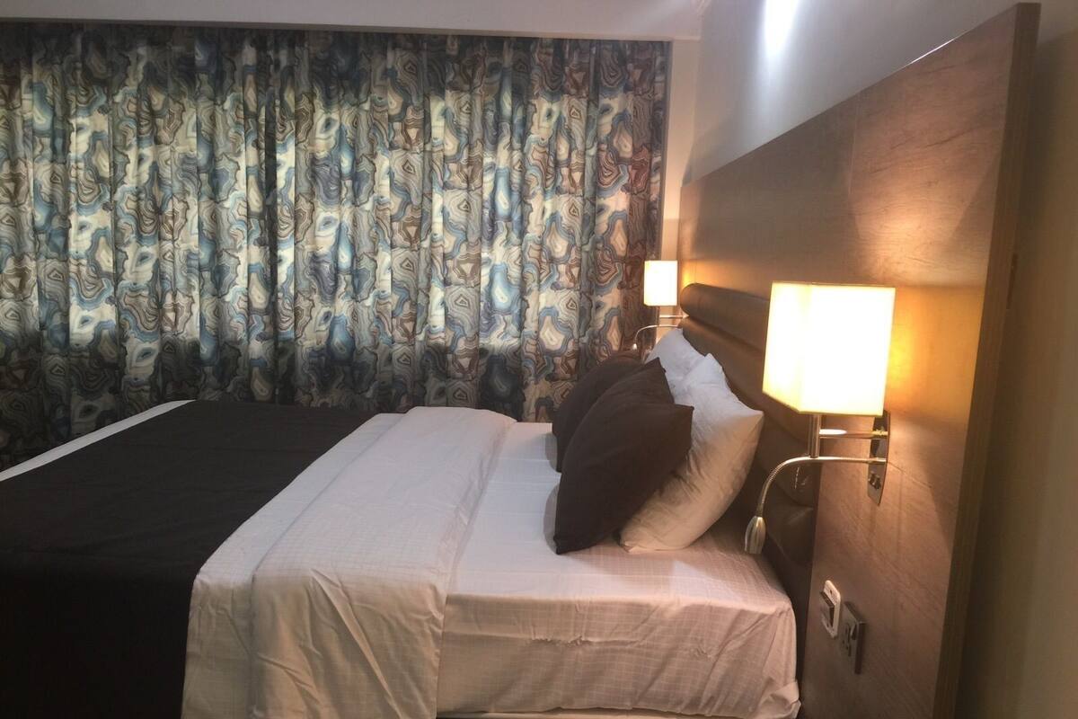 A hotel room with a bed, a nightstand with a lamp, and a curtain with a marble pattern.