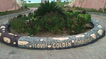 A circular stone pathway with the words "LOVE GOLDEN MARINA" engraved on it, surrounded by greenery and a view of the sea.