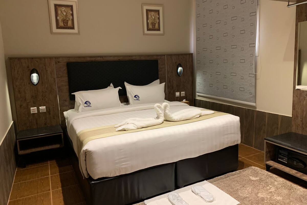 A neatly made bed with white linens and towels, a wooden headboard, and a small bedside table with a lamp.