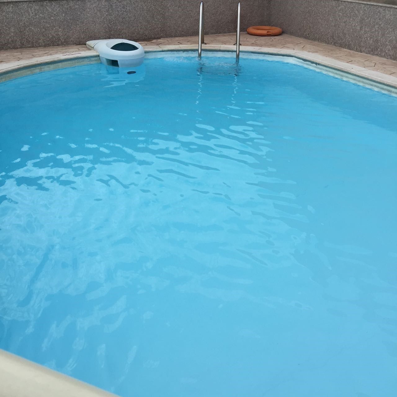 Una piscina con agua azul cristalina, un tobogán blanco y negro, y un flotador naranja pequeño.