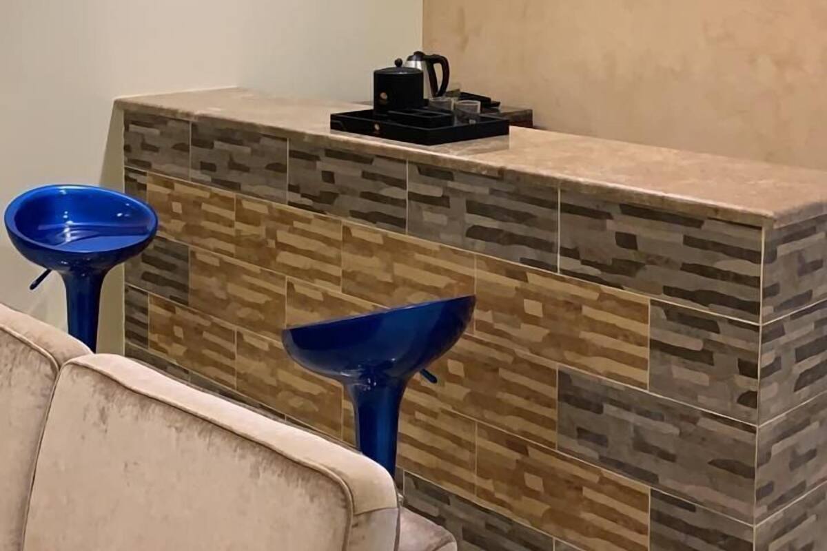A modern reception area with a stone-textured counter, two blue bar stools, and pendant lighting.