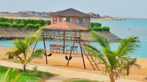 A beachside swing set with a small pavilion, palm trees, and a view of the sea. - Hotel & Resort Golden Marina Yanbu  فندق ومنتجع جولدن مارينا ينبع إدارة وتشغيل شركة منتجع المرسى الذهبي (Yanbu)