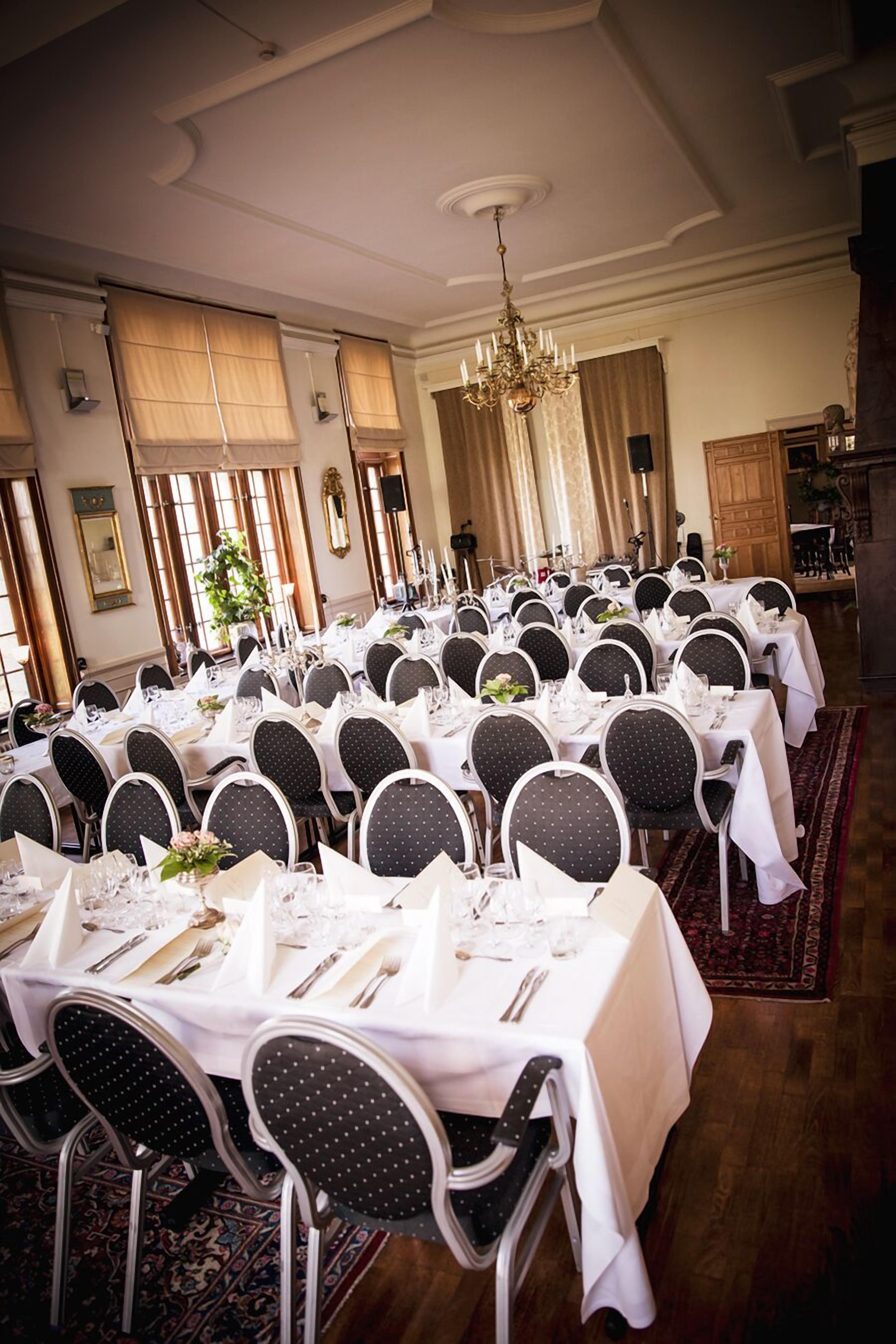 A banquet hall with round tables set for a formal event, featuring white tablecloths, black chairs, and a chandelier.