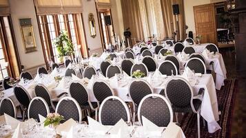 A banquet hall with round tables set for a formal event, featuring white tablecloths, black chairs, and a chandelier.