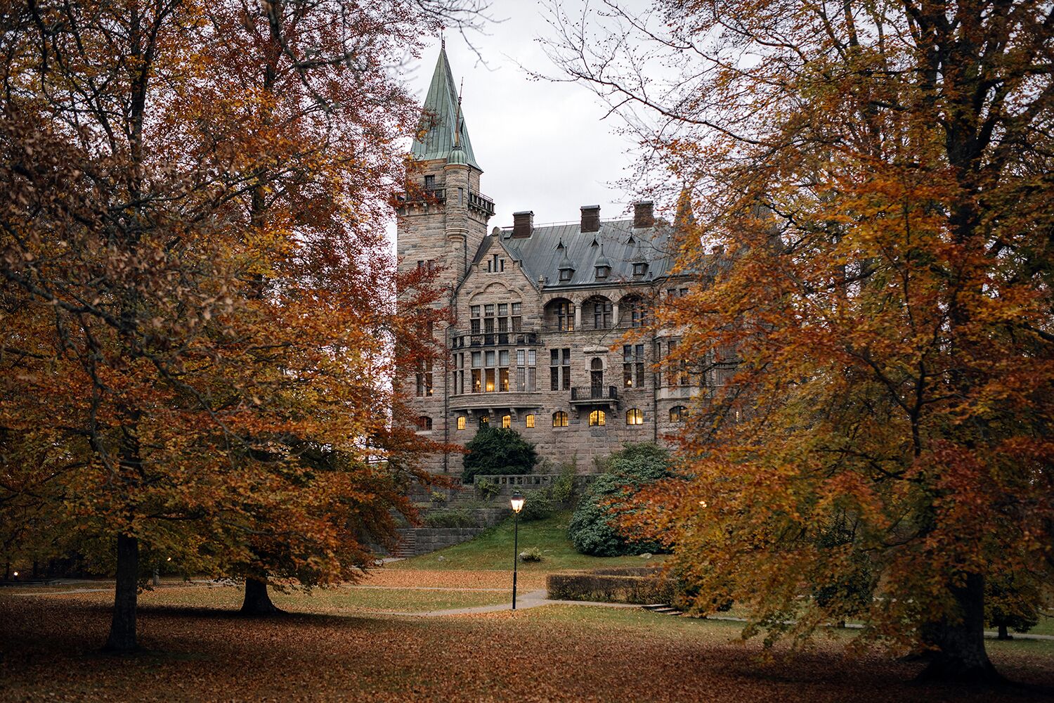 Een historisch gebouw met een opvallende toren en meerdere ramen, omringd door bomen met herfstkleuren.