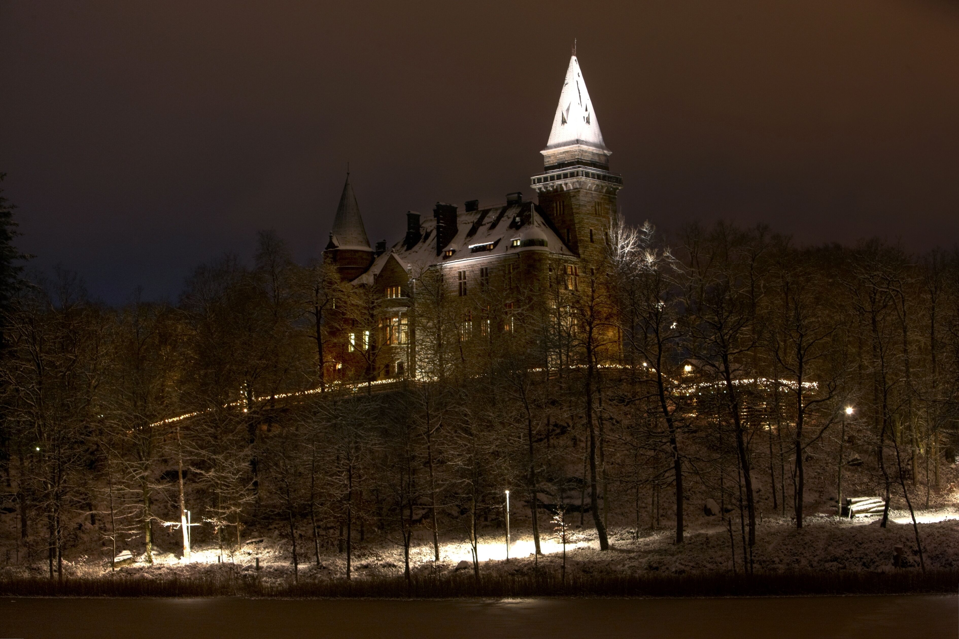 A historic building with multiple towers and a prominent spire, surrounded by a snowy landscape and trees.