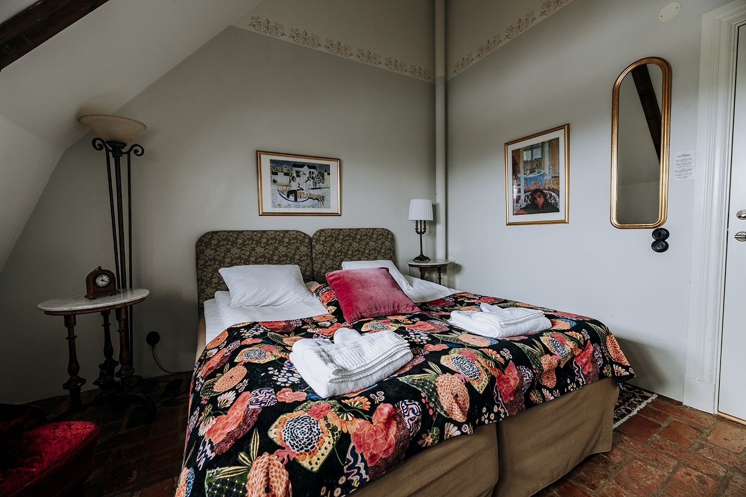 A bedroom with a bed, a nightstand, a lamp, a mirror, and a clock.