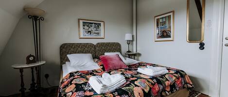 A bedroom with a bed, a nightstand, a lamp, a mirror, and a clock.