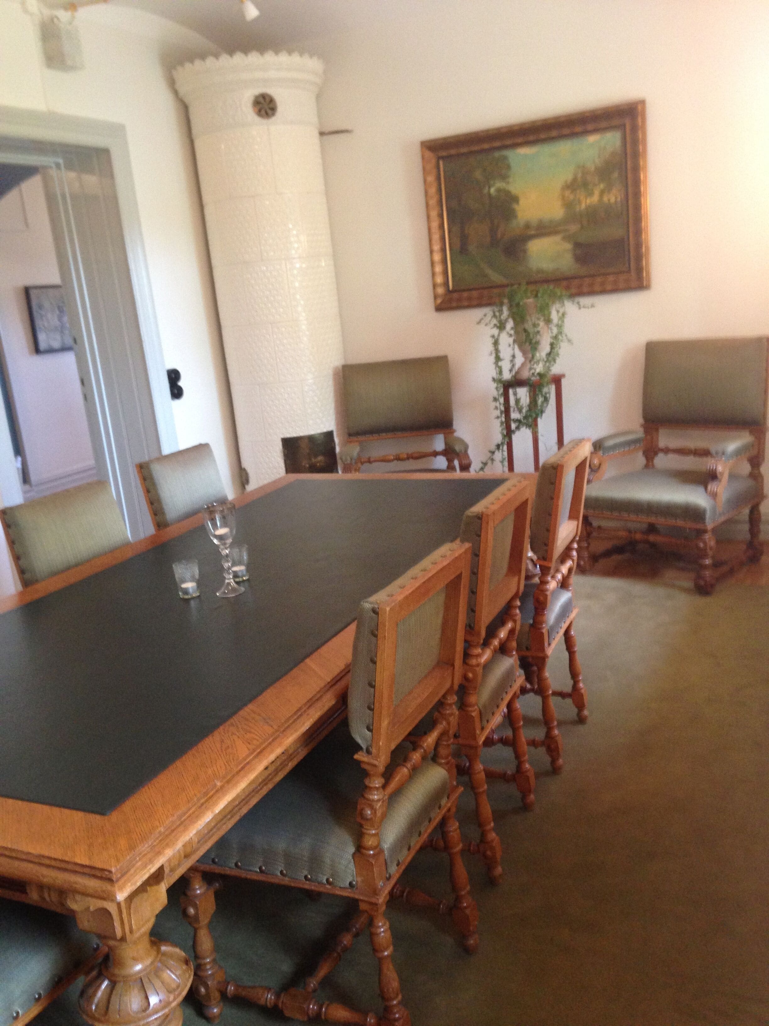 A conference room with a large wooden table, six upholstered chairs, a painting on the wall, and a decorative pillar.