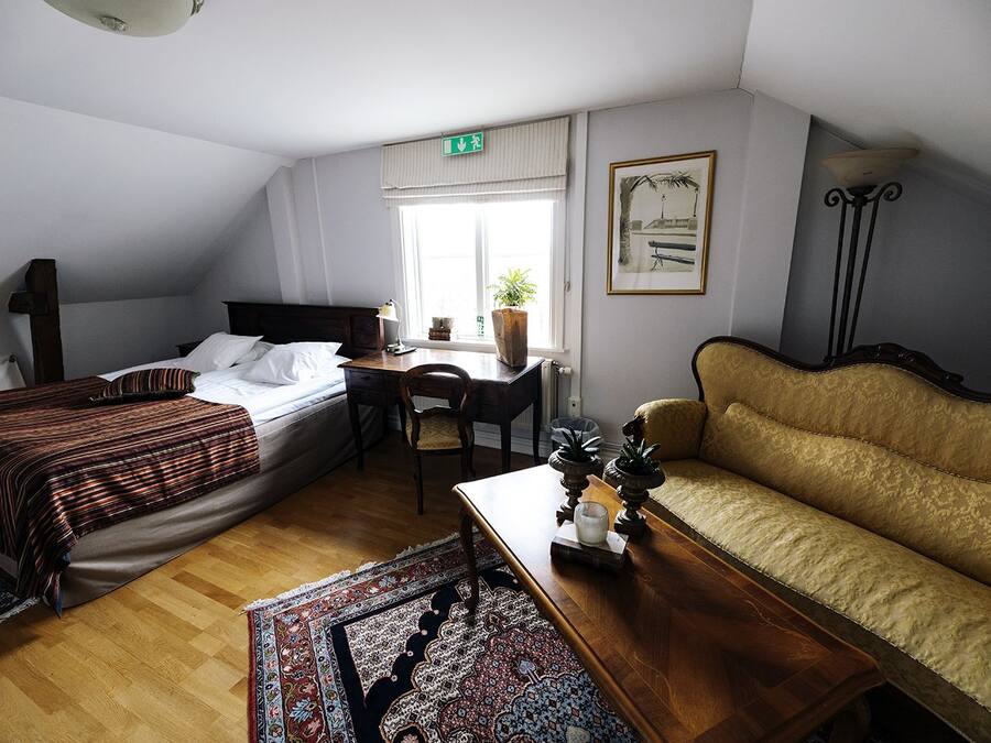 Una habitación con cama, escritorio, sofá y ventana con planta.