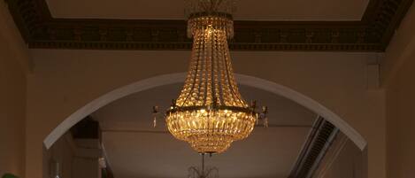 Un amplio pasillo con un gran ventanal arqueado, candelabros elegantes y muebles clásicos.