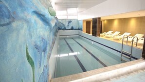 An indoor swimming pool with a mural of aquatic life on the walls, a diving board, and sun loungers. - The Ancient Mesopotamia Hotel (Batman)