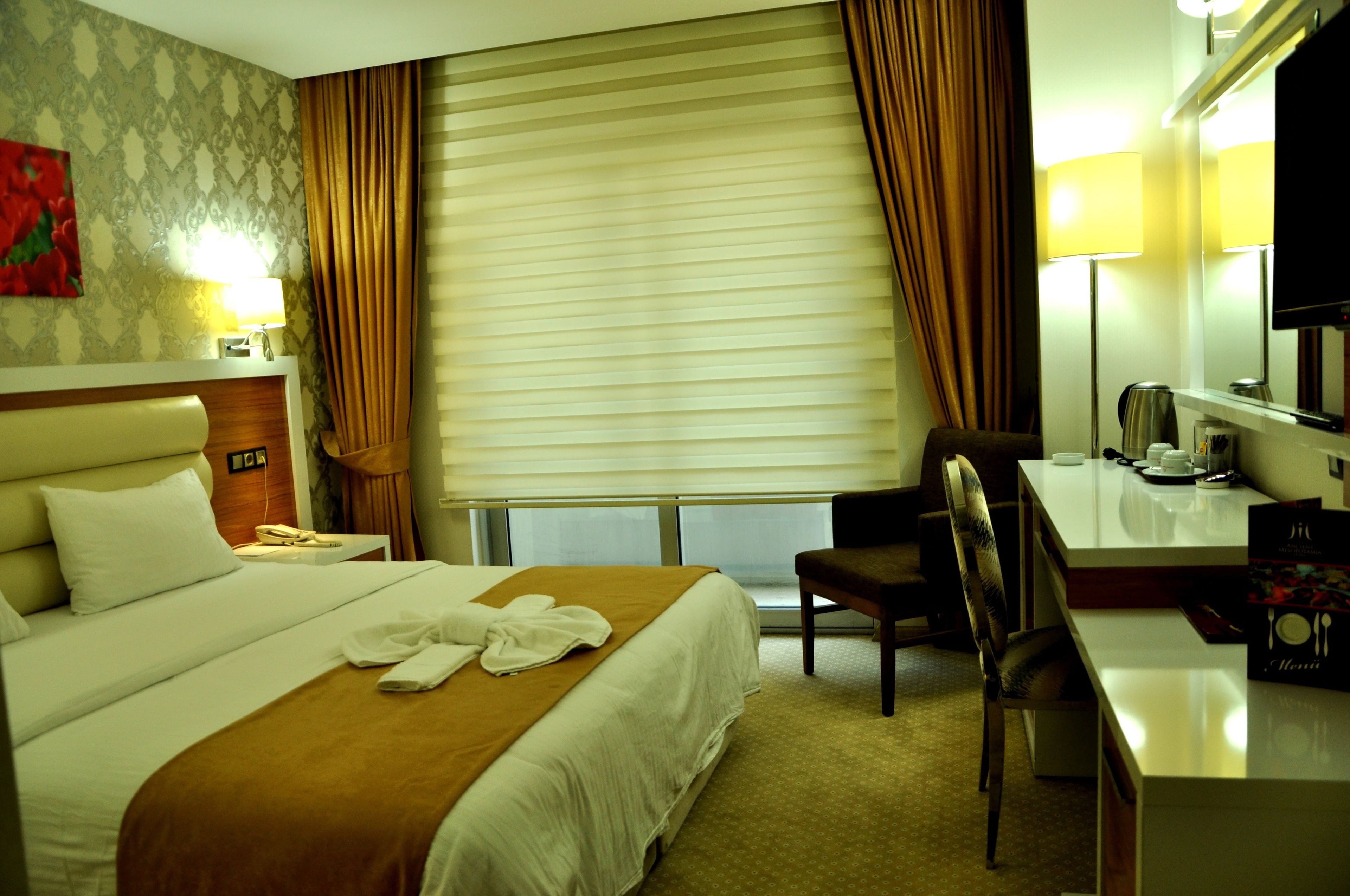 Habitación de hotel con cama, escritorio, silla, televisor y ventana con cortinas.
