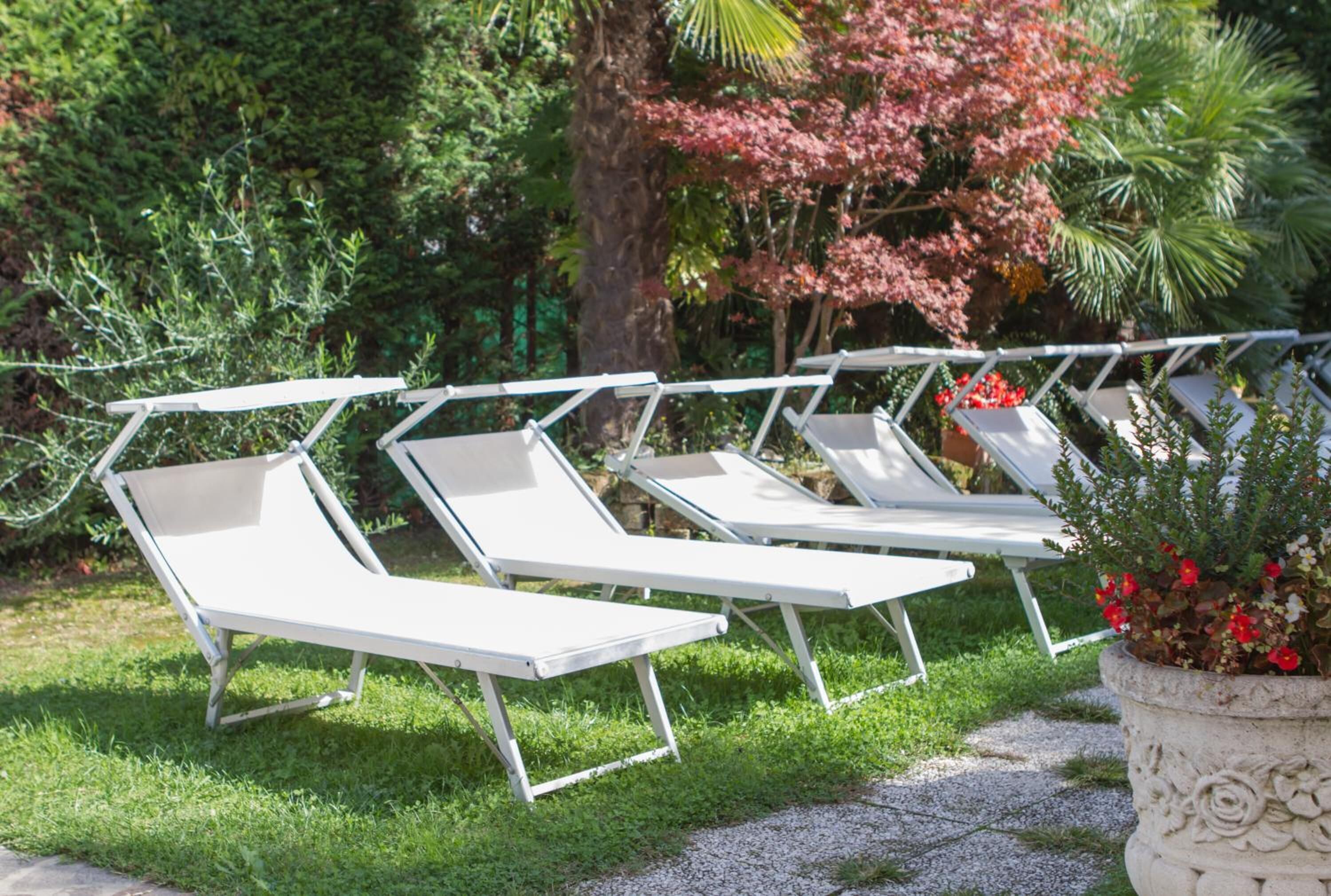 A row of white lounge chairs with metal frames, arranged on a grassy area with a gravel path.