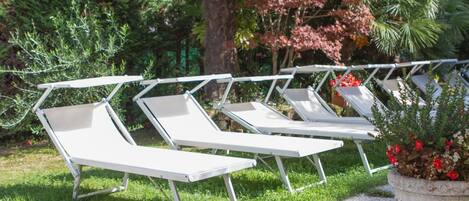 A row of white lounge chairs with metal frames, arranged on a grassy area with a gravel path.