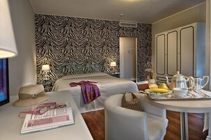 Quarto de hotel com papel de parede listrado em zebra, uma cama, um espaço de estar com uma bandeja de itens de café da manhã e um guarda-roupa.