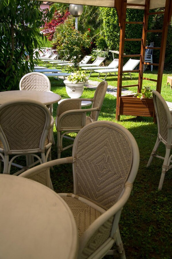 Un espacio de patio al aire libre con mobiliario de mimbre, una mesa blanca y una pérgola de madera.