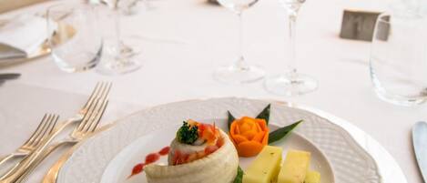 Una mesa de comedor dispuesta con un plato blanco, un recipiente pequeño de base verde y un adorno con una rosa.