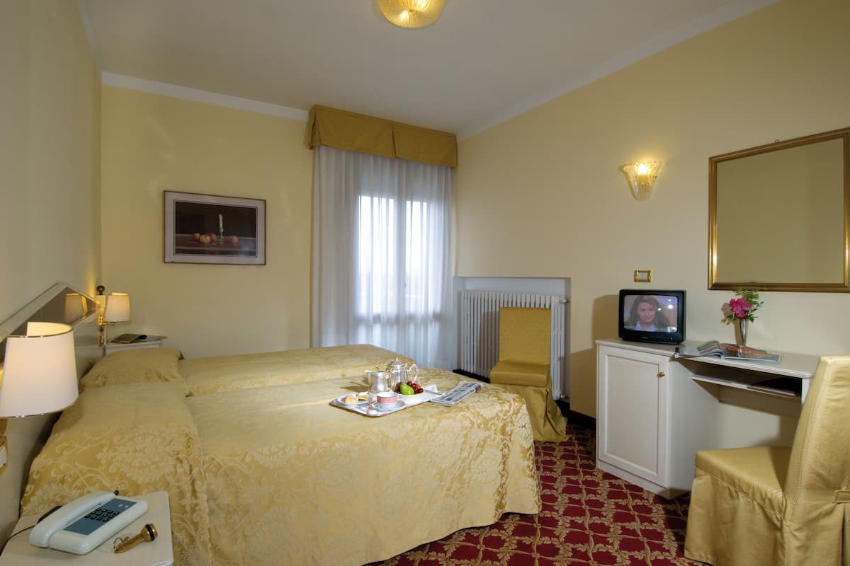 Quarto de hotel com cama, mesa de cabeceira, luminária, televisão e pequeno armário.