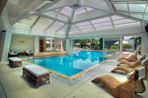 Una amplia piscina cubierta con sillones de descanso y techo de cristal.