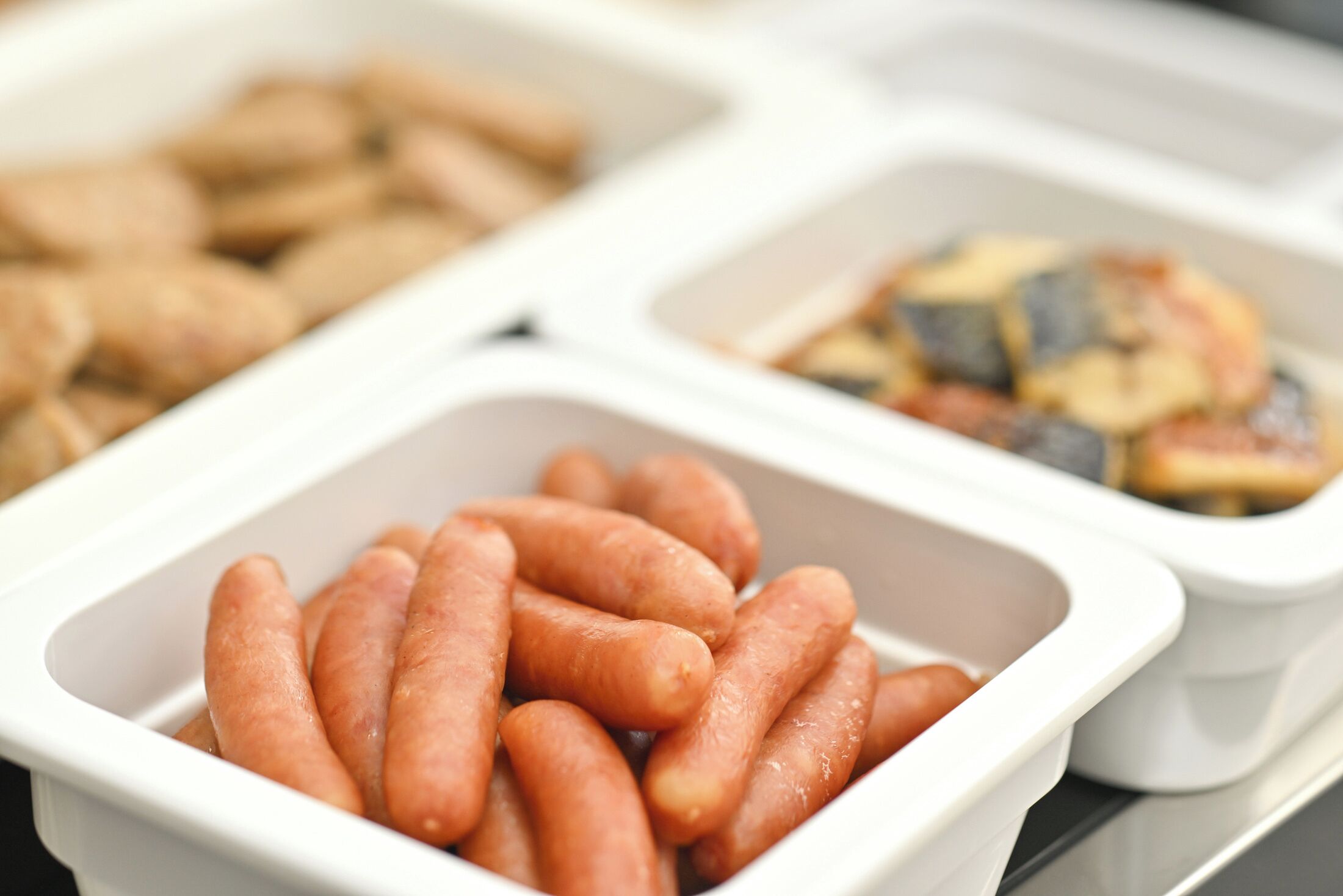A tray of food items including sausages and a dish with a yellow sauce.